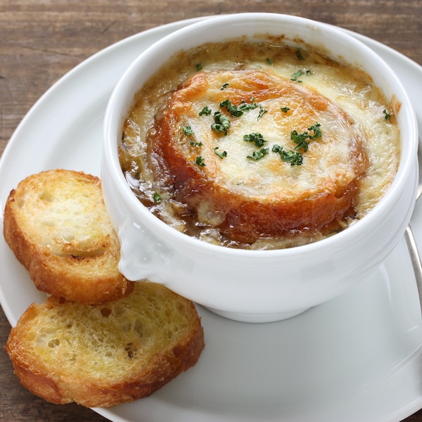 Une bol de soupe à l'oignon gratinée dans une assiette avec deux morceaux de pain.