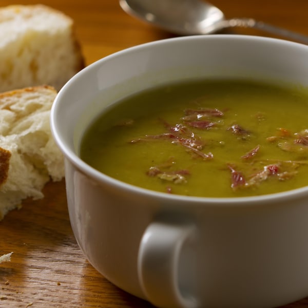 Un bol de soupe aux pois cassés et au jambon, servi avec du pain croûté et une cuillère.