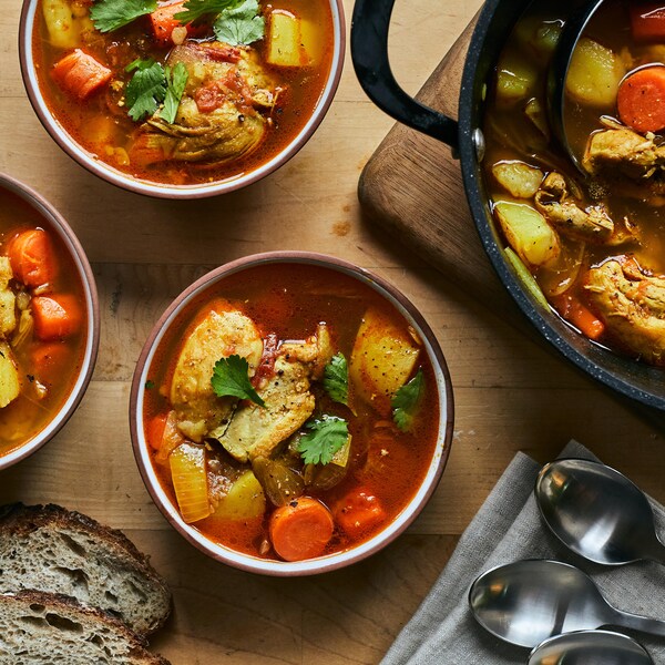 Trois bols et une cocotte contenant la soupe au poulet et aux épices brésiliennes sur une table de bois.
