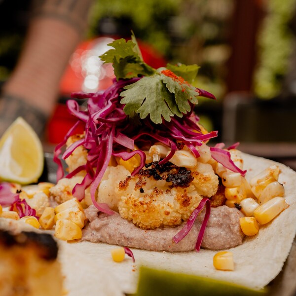 Un taco contenant des morceaux de chou-fleur grillés, du chou rouge émincé, des grains de maïs et de la purée de cajou.