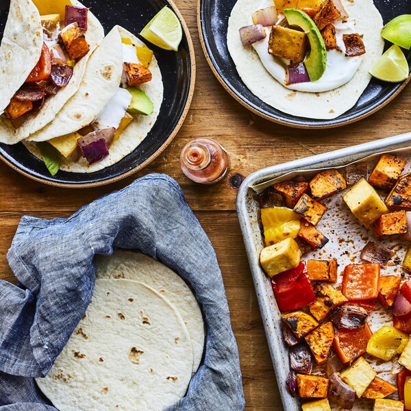 Tacos végé à la plaque dans deux assiettes et légumes sur une plaque.