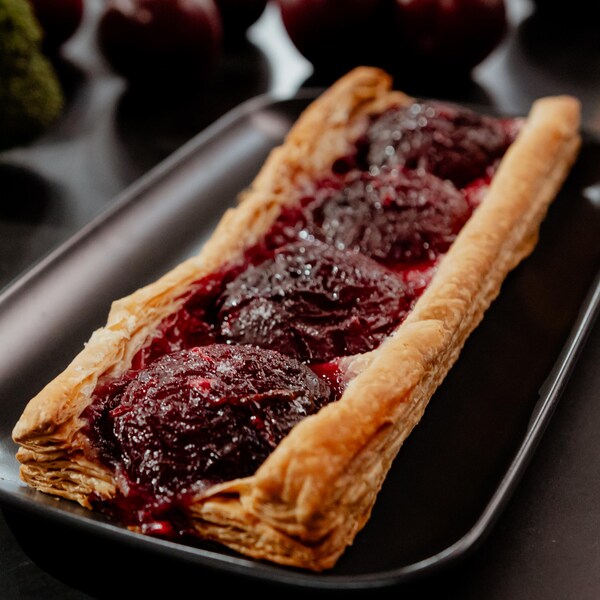 Une tarte feuilletée aux prunes de forme rectangulaire, dans une assiette.