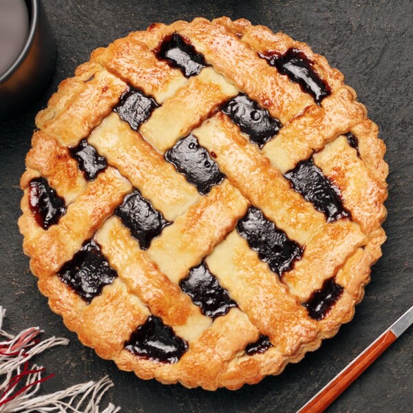 Une tarte aux mûres déposée sur une table avec une fourchette, un couteau et deux tasses de café.