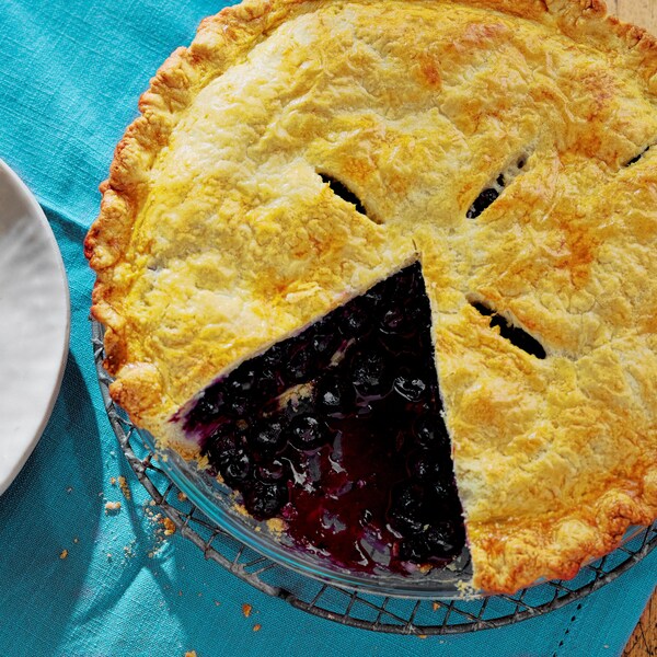Un morceau de tarte aux bleuets dans une assiette et le restant de la tarte sur un comptoir.