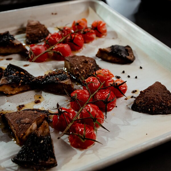 Des tomates cerises et des morceaux de champignons portobellos sur une plaque de cuisson sortant du four.