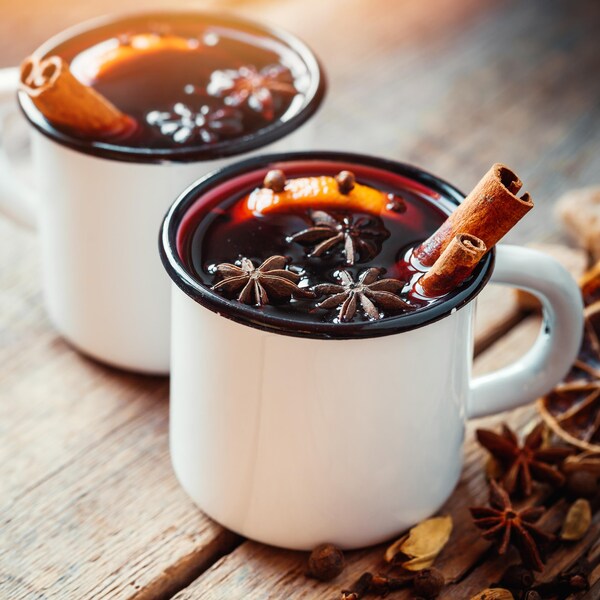 Deux tasses blanches contenant du vin rouge et plusieurs épices.