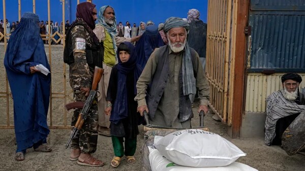 A Taliban fighter stands guard as people receive food rations distributed by a South Korean humanitarian aid group, in Kabul, Afghanistan, on May 10. World Vision says it was forced to cancel a recent food shipment to the Taliban-run country because of a Canadian law banning dealings with terrorists. (Ebrahim Noroozi/The Associated Press)
