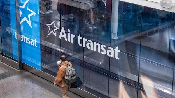 Un voyageur marche devant un logo d'Air Transat à l'aéroport Montréal-Trudeau.