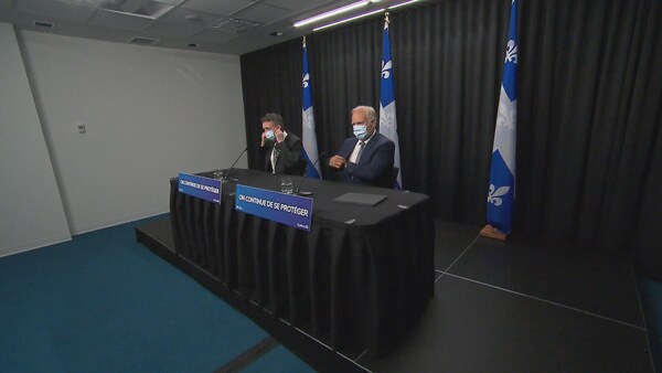 Deux responsables, dont le Dr Luc Boileau, portent le masque et sont assis à la table d'une conférence de presse.