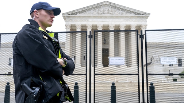 Un policer armé, les bras croisés, devant la Cour suprême, protégée par un grillage. 