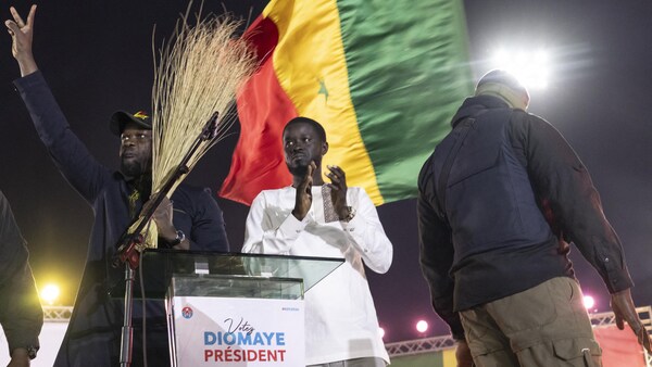 Deux hommes applaudissent et font le signe de la victoire et derrière eux flotte un drapeau géant du Sénégal. 