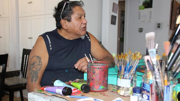 Frank Polson est assis à sa table de travail, entouré de pinceaux et de tubes de peinture.