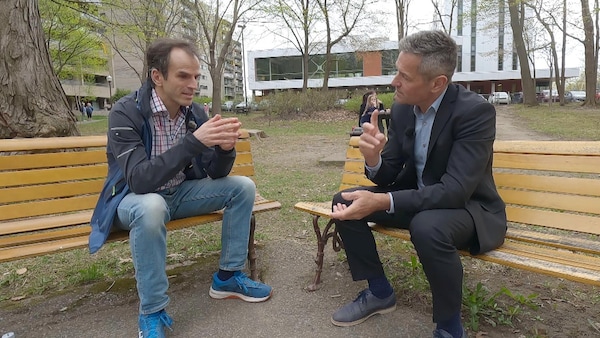 Deux hommes discutent, assis sur un banc de parc, au printemps. 