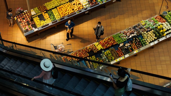 Des gens magasinent dans le rayon des fruits d'une épicerie.