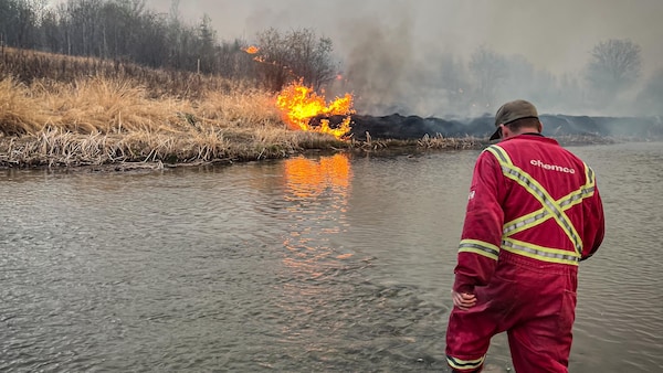 Un pompier traverse une rivière vers et se dirige vers un feu, en Alberta, au mois de mai 2023.
