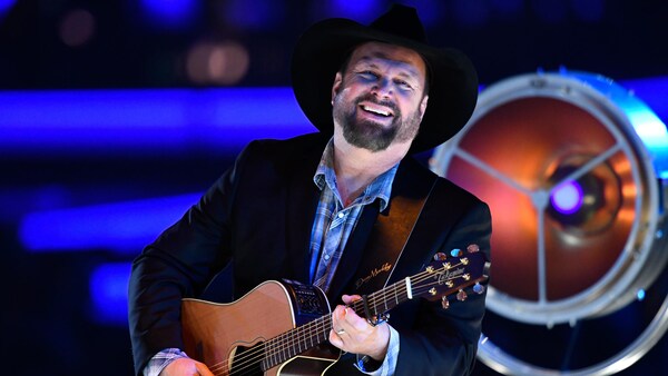 Garth Brooks, vêtu d'un chapeau de cowboy et d'un veston noir, jouant de la guitare sur scène.