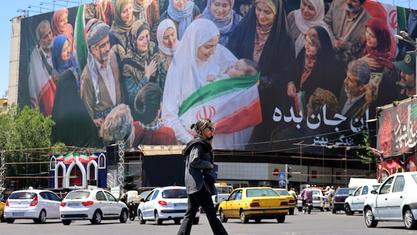 Une femme traverse une rue devant un grand panneau d'affichage politique près de la place Enghelab, dans le centre de Téhéran, le 26 mai 2026.