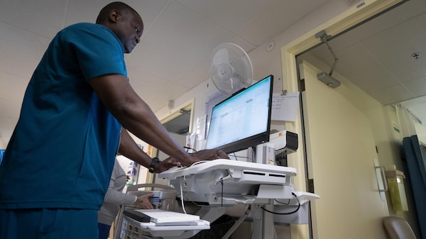 Un infirmier de profil travaille sur un ordinateur dans le corridor d'un hôpital.