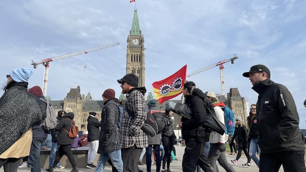 Des personnes manifestent devant le parlement à Ottawa, le matin du vendredi 21 avril 2023, au troisième jour de la grève des fonctionnaires fédéraux. Une personne tient un drapeau de l'Alliance de la Fonction publique du Canada.