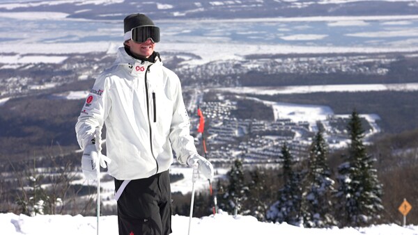 Un jeune homme sourit dans une pente de ski devant le fleuve gelé. 