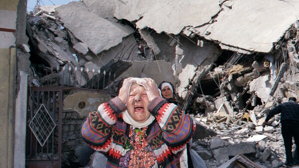 Une femme se prend la t&ecirc;te et pleure devant un immeuble en ruines.