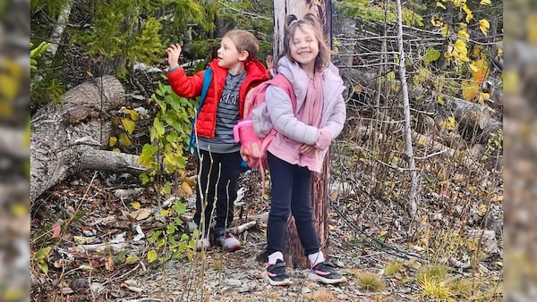 Des enfants de 4 et 6 ans dans la forêt. La petite fille sourit, les yeux plissés. Le petit garçon, un pas derrière, regarde vers la gauche de l'image.