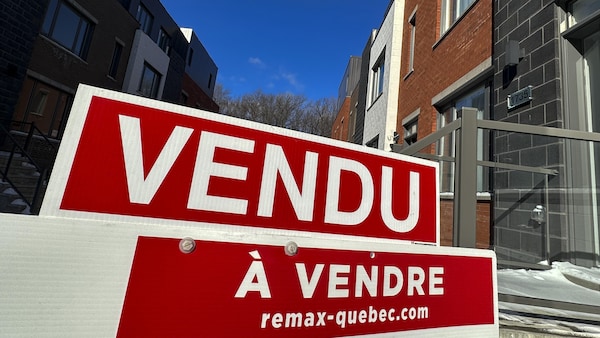 Une pancarte « Vendu » devant un immeuble résidentiel.