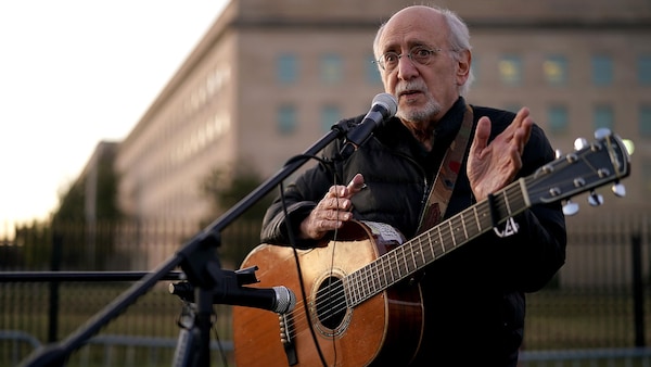 L'homme parle dans un micro, sa guitare accrochée en bandouilère. 