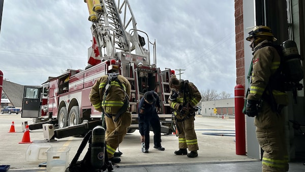 Des pompiers attachent leur équipement derrière un camion de pompier. 