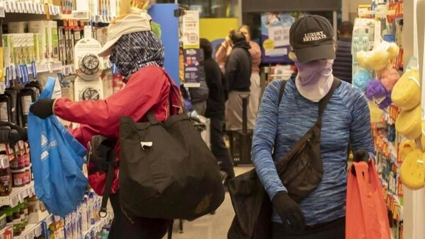 Des personnes dont le visage est caché mettent des articles dans des sacs, dans une allée d'épicerie.