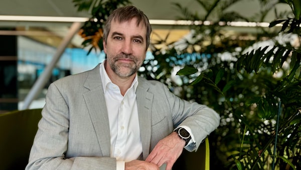 Steven Guilbeault, un homme en veston gris et en chemise blanche, pose devant des plantes vertes dans un espace lumineux.