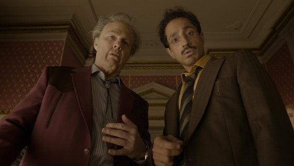 Les deux hommes sont dans un salon et regardent vers le bas. 