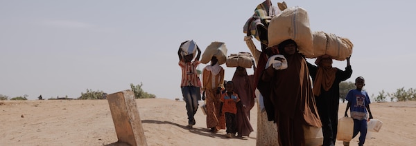 Des gens marchent dans le désert en portant des sacs en jute sur la tête.