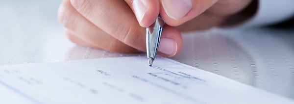 Une main tenant un stylo signe un chèque.