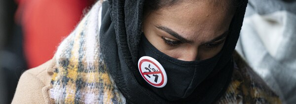 Une femme porte un couvre visage sur lequel est épinglé un macaron contre la loi 21.
