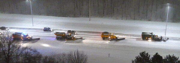 Des véhicules tentent de dépasser les multiples chasse-neige alignés sur l'autoroute alors qu'il neige.