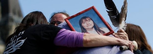 Quatre personnes se serrent dans les bras en portant la photo d'une femme.