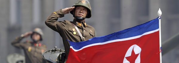 On voit un soldat dans un tank qui fait le salut militaire. Devant lui, le drapeau nord-coréen.