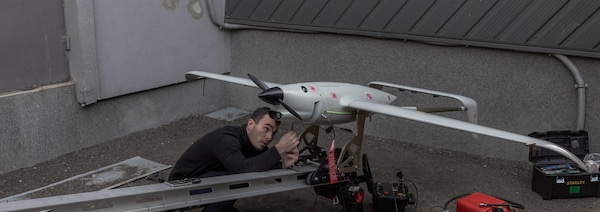 Une homme travaille sur un drone au sol.