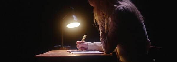 Une femme écrit dans un écrit près d'une lampe. 