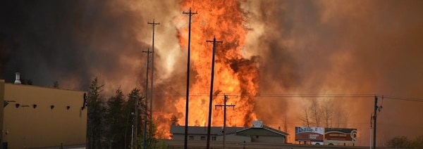 Des flammes montent jusqu'au ciel devant une maison et ce qui ressemble à une zone industrielle. 