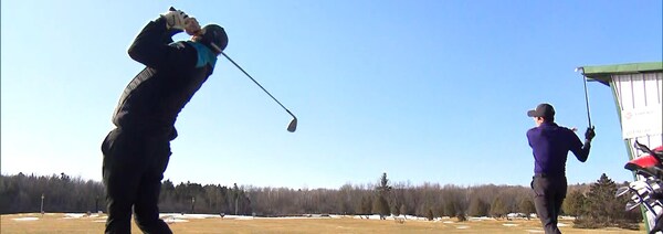 Deux golfeurs s'exercent sur un champ de pratique sur un terrain où subsistent quelques amoncellements de neige.