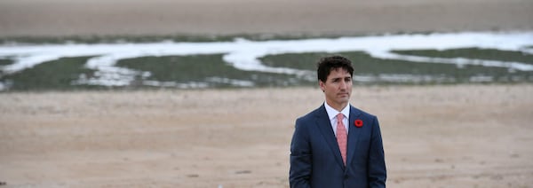 Justin Trudeau portant un coquelicot et prenant une pose solennelle sur la plage, tandis qu'on voit de l'eau et des vagues à l'arrière.