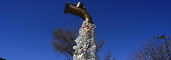 Un gros robinet déverse un flot de bouteilles, de contenants et d'emballages en plastique.