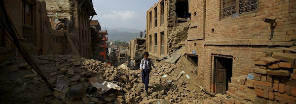Un écolier en uniforme marche entre les ruines des maisons. 