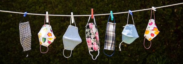 Des masques de différentes couleurs et de différents formats accrochés sur une corde à linge.