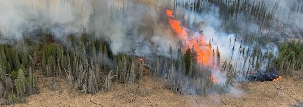 Feu de forêt avec fumée et flammes, près d'une rivière, le 15 mai 2023, à Hay River, aux Territoires du Nord-Ouest.