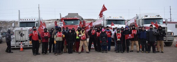 Deux douzaines de personnes habillées très chaudement et portant les couleurs du syndicat Unifor debout devant des camions-citernes.