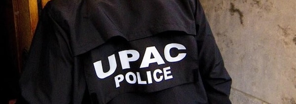 Un enquêteur de l'UPAC dont on voit l'uniforme de dos.