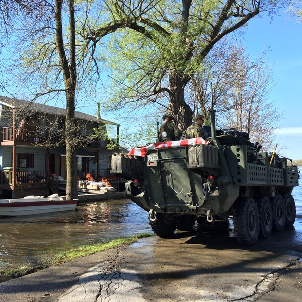 Arrivée d'un groupe de militaires des Forces armées canadiennes dans le secteur inondé de la rue Fournier, à Saint-André-d'Argenteuil; on voit une maison et un bateau en arrière-plan.